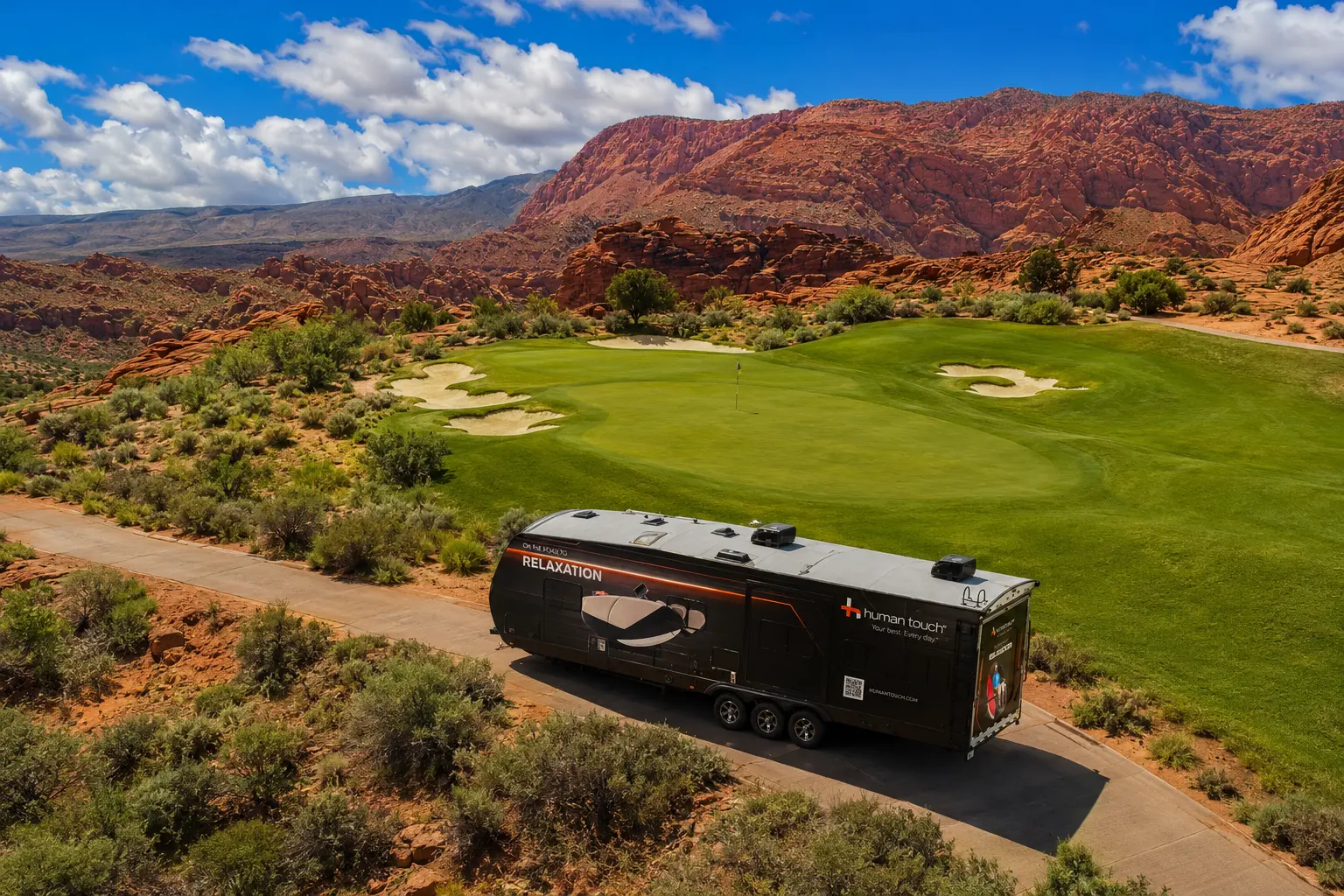 Aerial view of the Human Touch Recovery Lounge trailer parked beside a golf course green with red rock mountains in the background